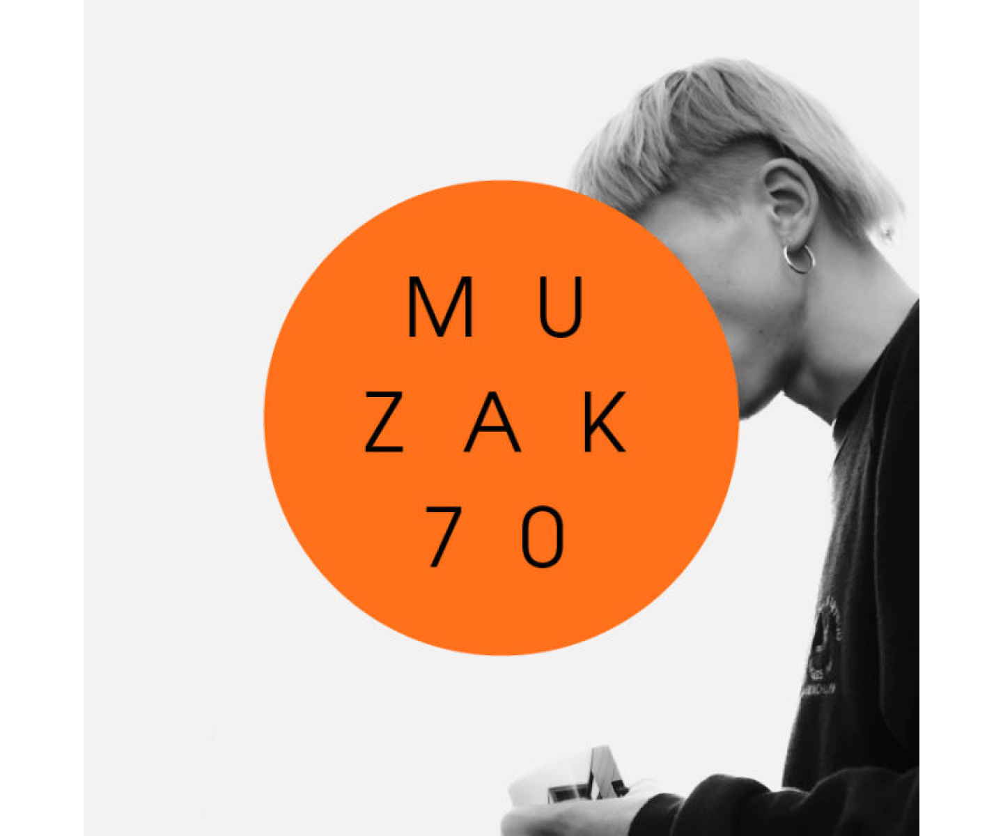 The image shows a person with light-coloured hair looking down. A large orange circle with the text "MUZAK 70" is placed over their face. The image is in black and white, except for the orange circle. The person is holding something in their hands.